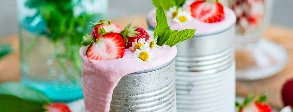 two tin cans with strawberry milkshakes in them with fresh strawberries and herbs on top