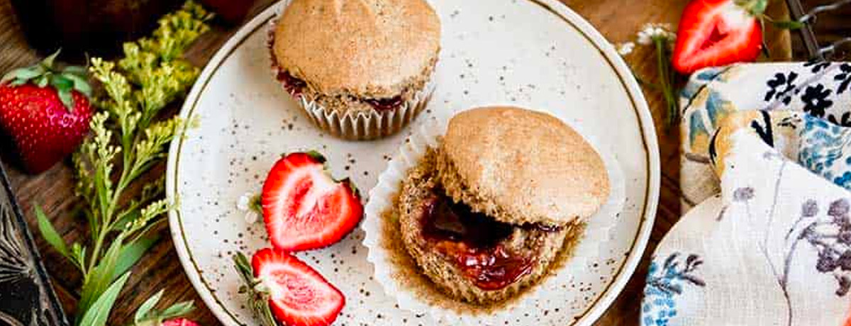 two muffins on a plate with fresh strawberries, colorful napkins, and a stem of small flowers