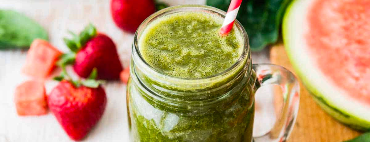 green smoothie with a red straw and fresh watermelon and strawberries next to it