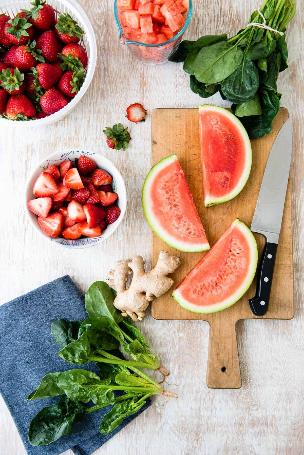 sliced watermelon, strawberries, whole ginger root and spinach leaves getting prepped for a smoothie.