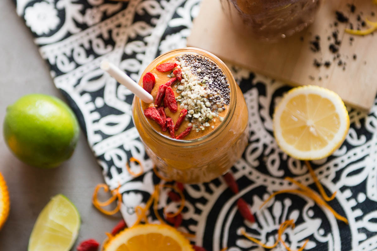 superfood smoothie in glass jar topped with goji berries, hemp hearts, chia seeds and a white paper straw.