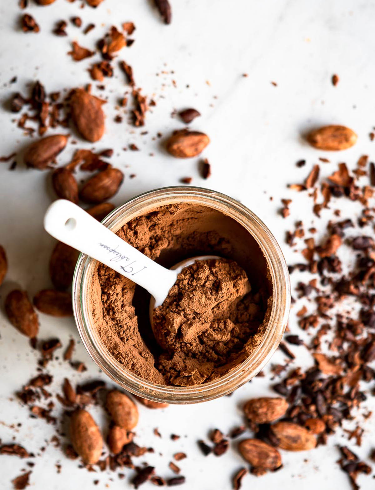 superfood cacao powder in a glass jar, getting scooped by a white tablespoon.