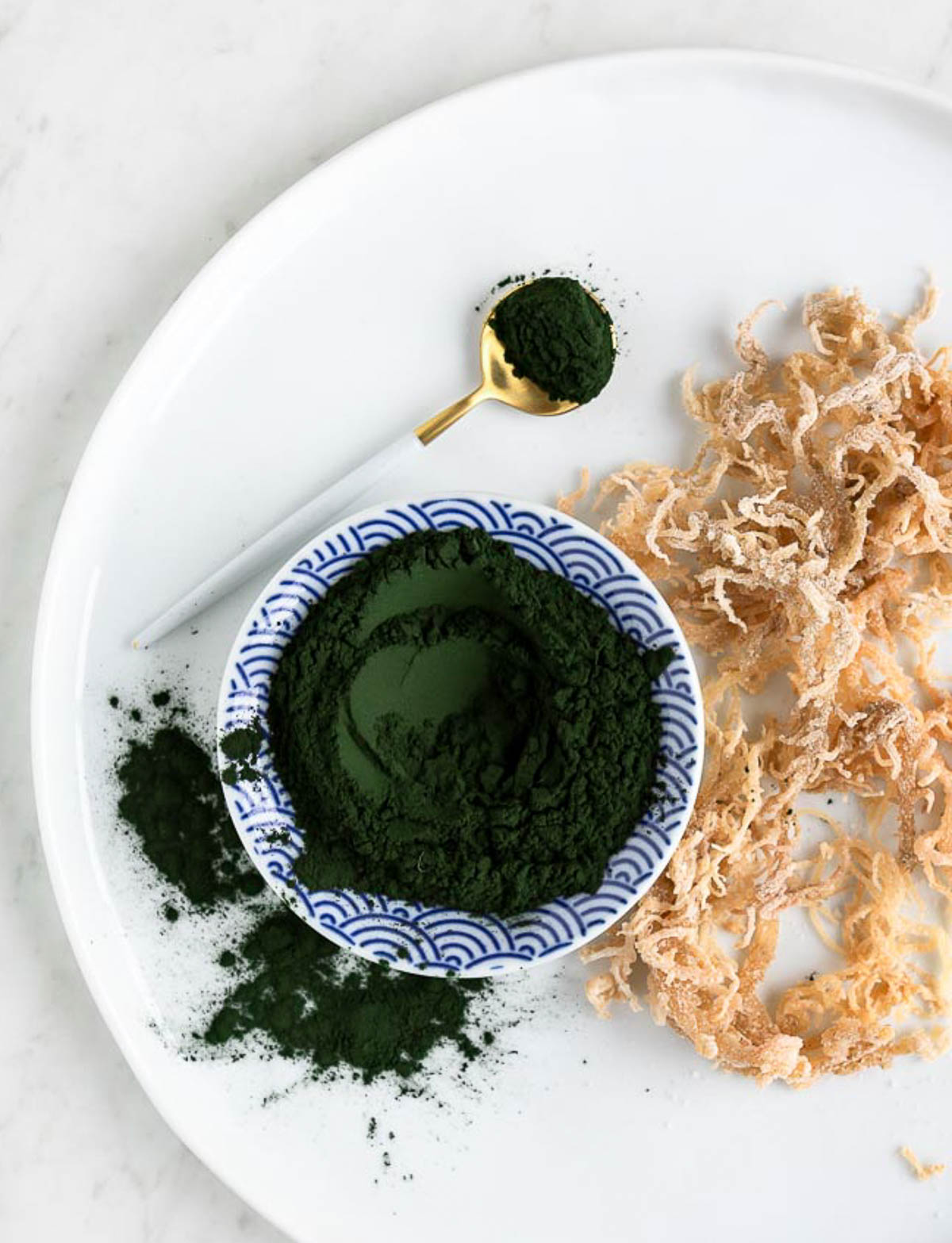 white bowl with blue lines filled with green algae powder, next to several strings of sea moss.