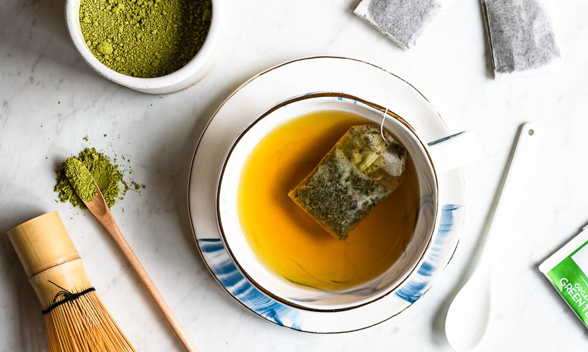 tea cup on a plate with green tea steeping, next to a containers of green tea powder. 