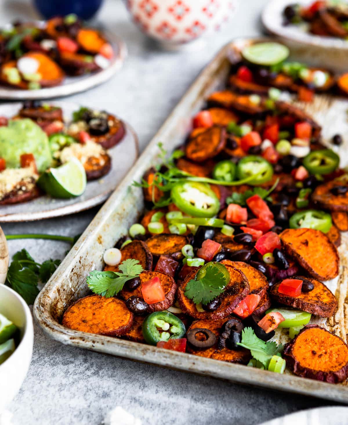 gorgeous tray of nachos topped with jalapeños, cilantro, olives, and tomatoes, all plant based ingredients.