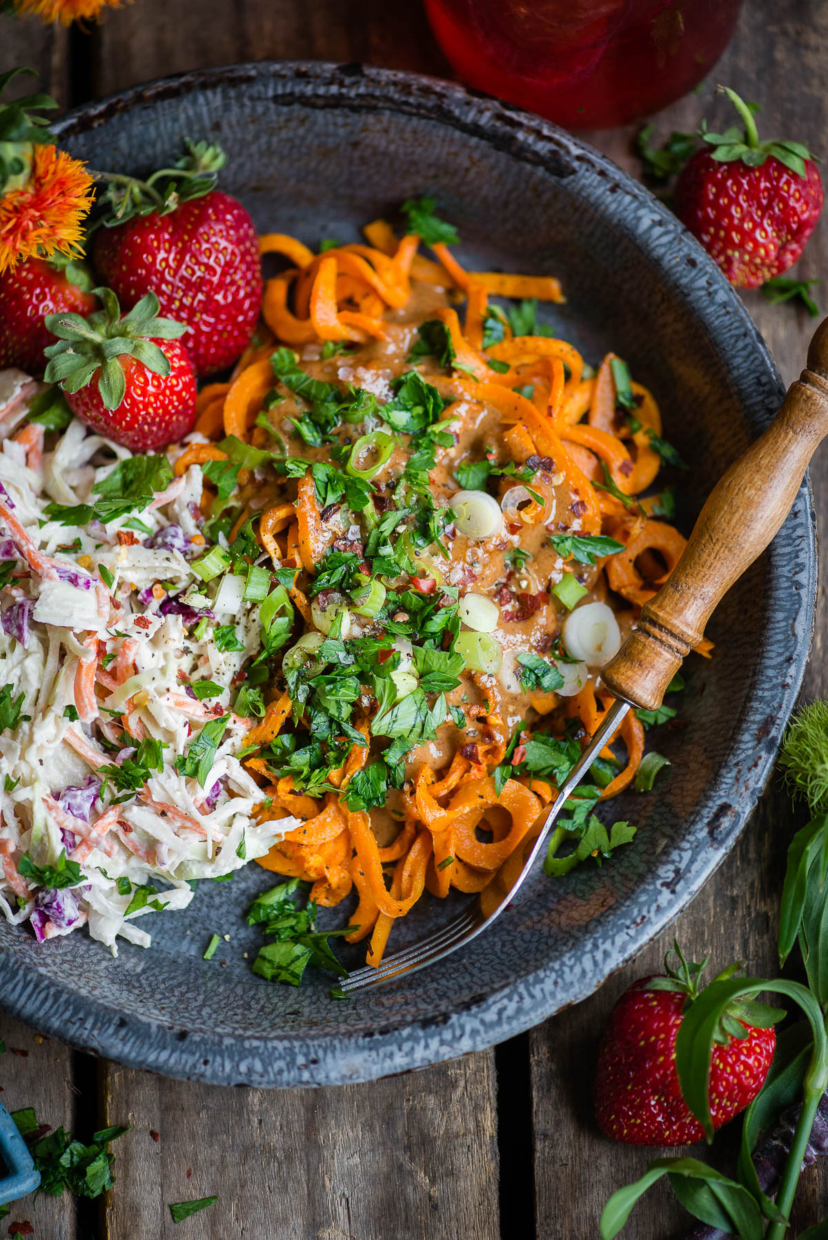 Bowl of gluten-free noodles made from sweet potatoes and topped with coleslaw and fresh strawberries. Wooden fork on the side.