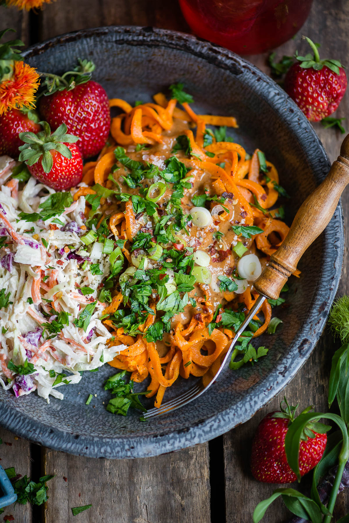 Bowl of Sweet Potato Noodles topped with vegan coleslaw and fresh strawberries, served with a wooden handled fork.