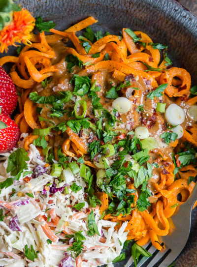gray bowl of sweet potato noodles topped with a vegan coleslaw and some whole strawberries.