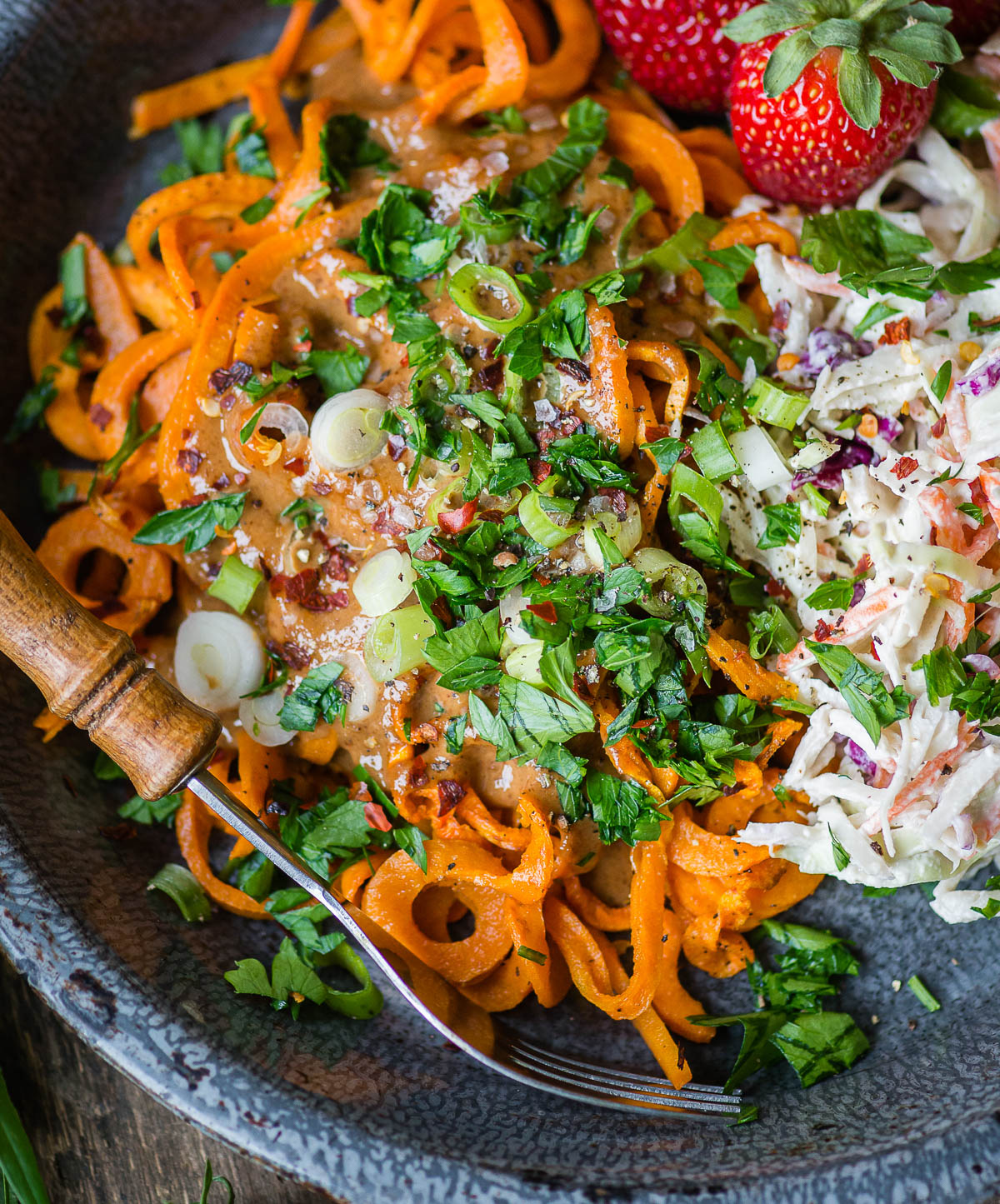 Healthy sweet potato noodles recipe featuring savory noodles topped with parsley, chives, and coleslaw with a wooden-handled fork.