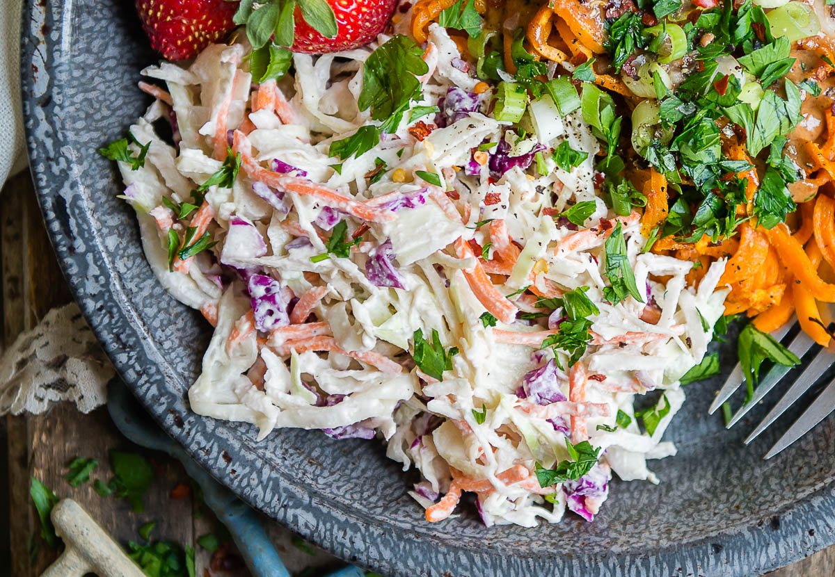 vegan coleslaw in a bowl with sweet potatoes and parsley.