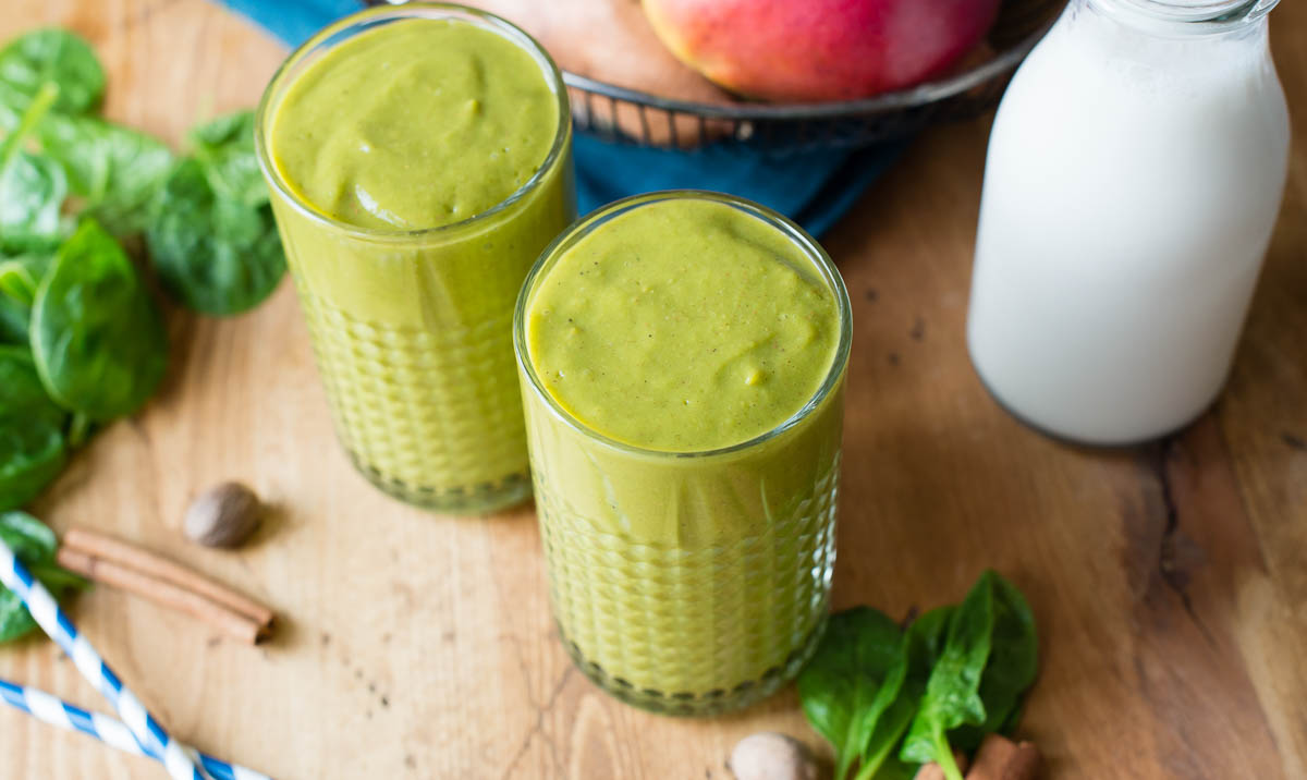 2 glasses of green smoothie on a wooden table.