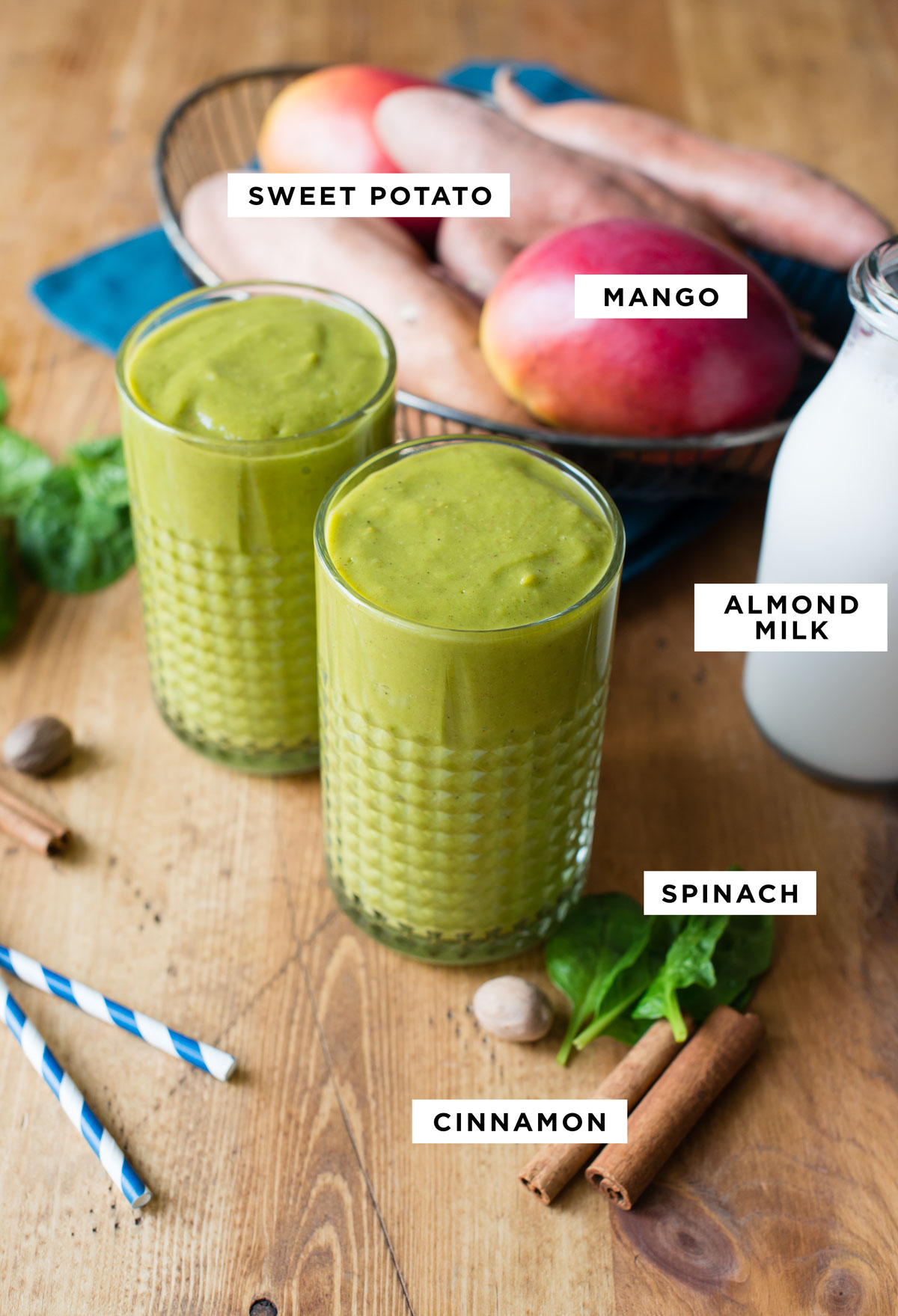 A collection of labeled ingredients for a sweet potato smoothie are neatly arranged. These include diced sweet potato, mango, almond milk, spinach leaves, and ground cinnamon. 