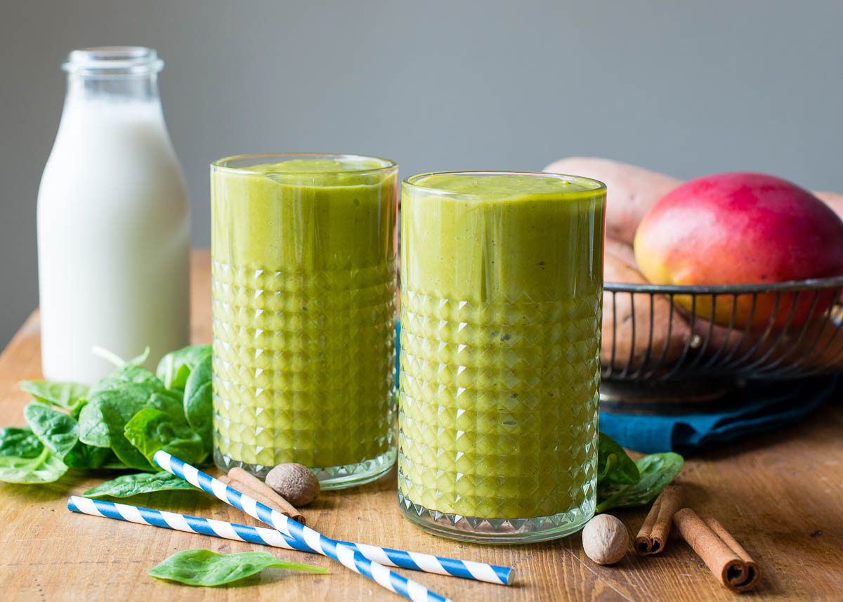 Glasses of sweet potato smoothie on a table with fresh spinach and cinnamon sticks nearby.