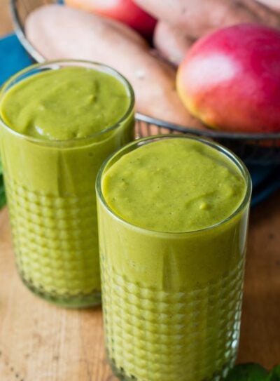 Two glasses of sweet potato smoothie on a table with fresh ingredients.