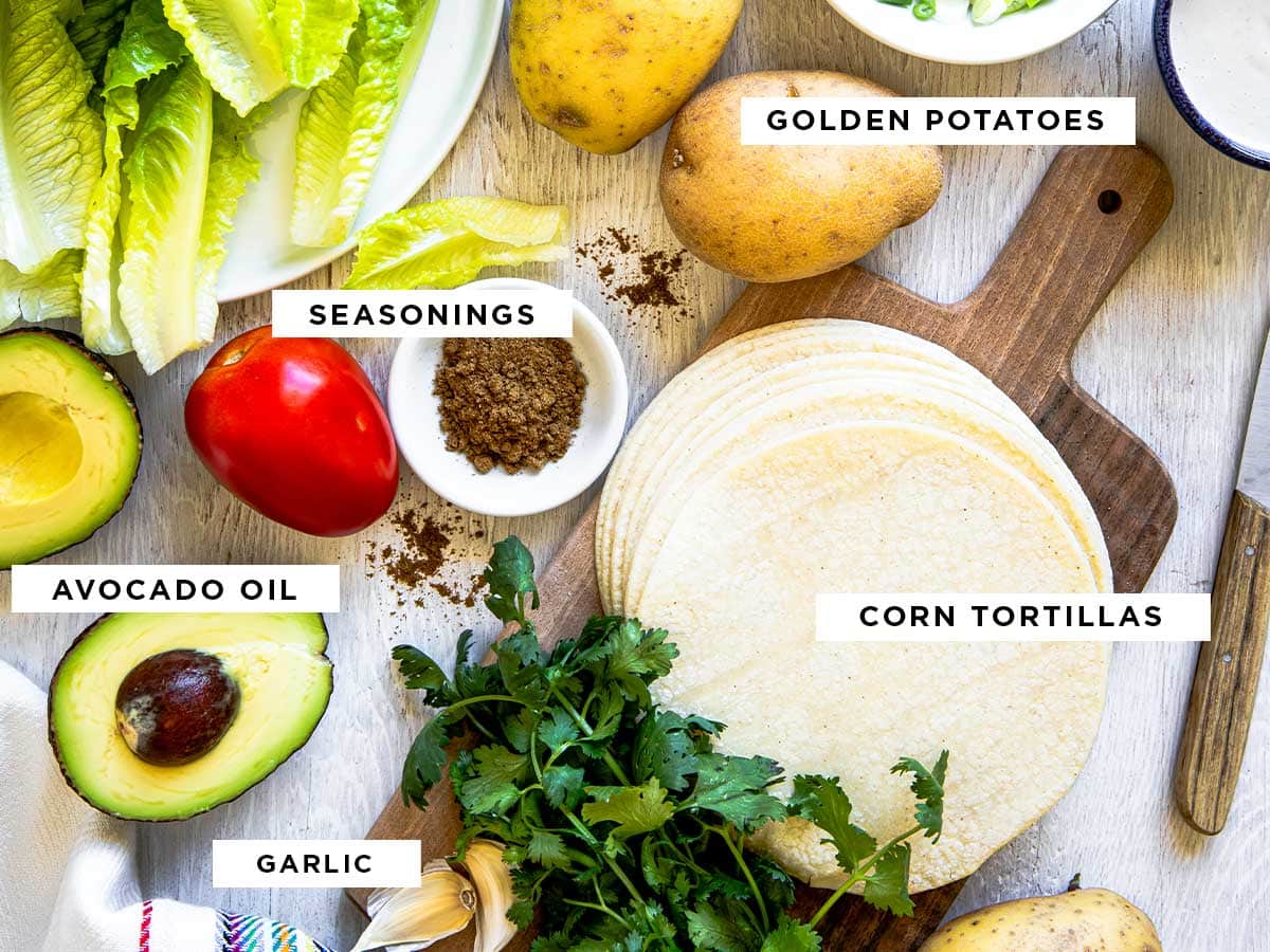 ingredients for crispy potato tacos including golden potatoes, seasonings, corn tortillas, avocados and garlic.