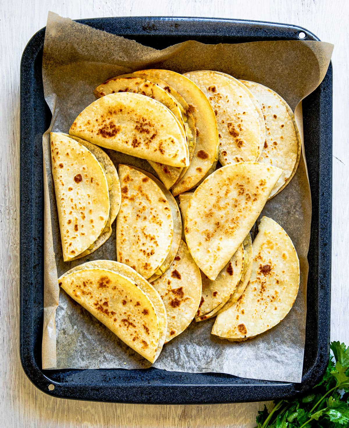 A pan full of freshly fried tacos de papa overlapping each other on parchment paper.