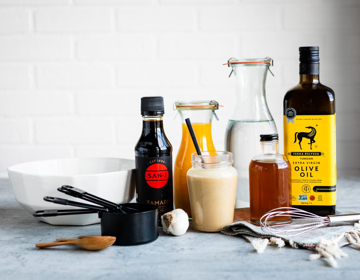 tahini dressing in clear glass jar surrounded by ingredients used to make this recipe.