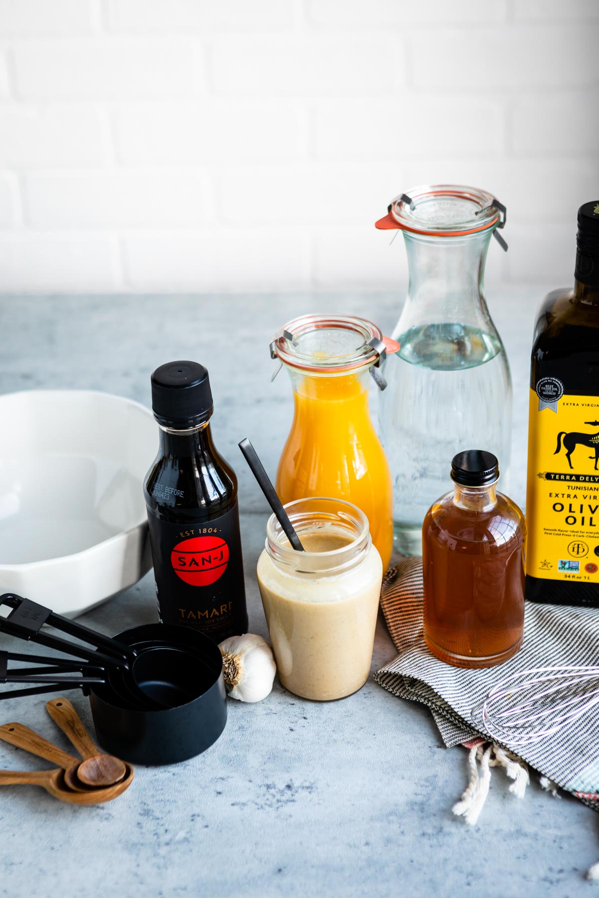 ingredients for a nut free dressing including tamari, tahini, orange juice, apple cider vinegar, olive oil and garlic cloves.