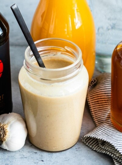 tahini dressing in a glass jar surrounded by tamari, orange juice, and maple syrup.
