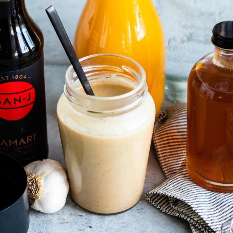 tahini dressing in a glass jar surrounded by tamari, orange juice, and maple syrup.