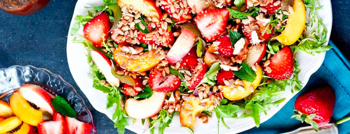 big salad plate with leafy greens, peaches, strawberries, crunchy toppings, and dressing