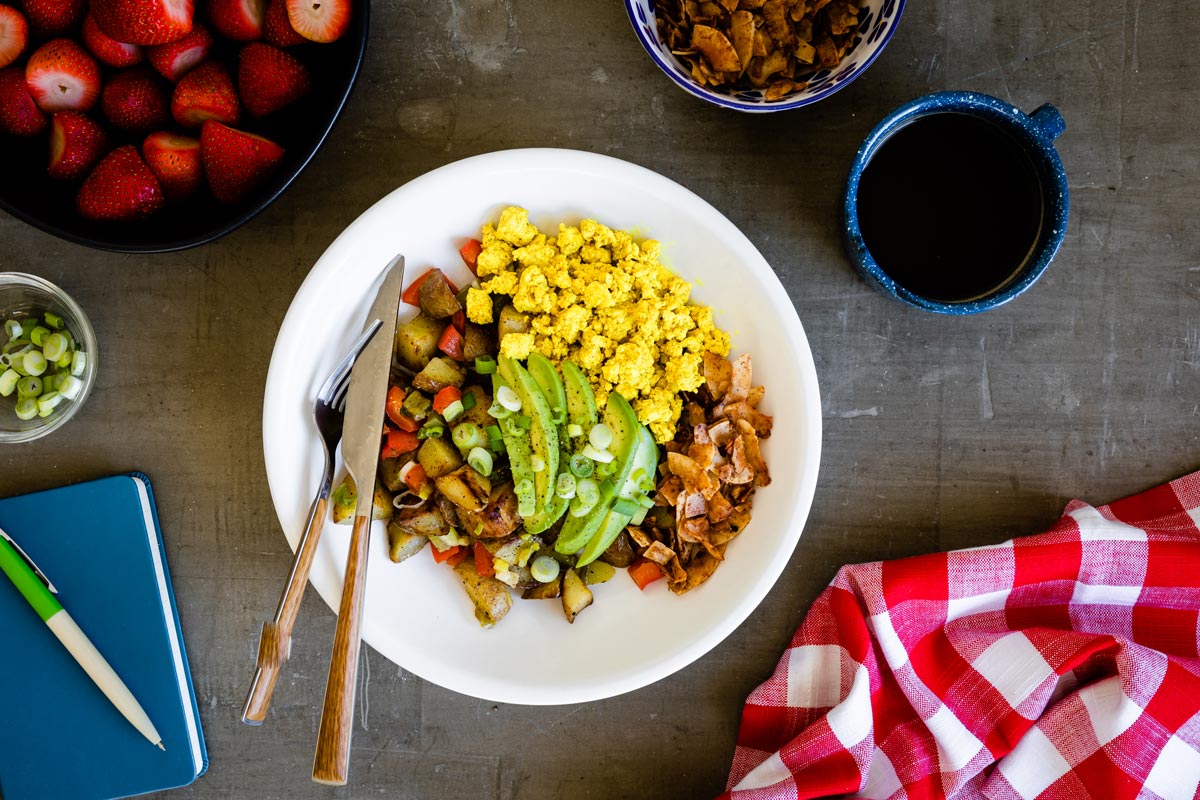 A delicious, vegan breakfast bowl with tofu, coconut bacon, sliced avocados and potatoes.