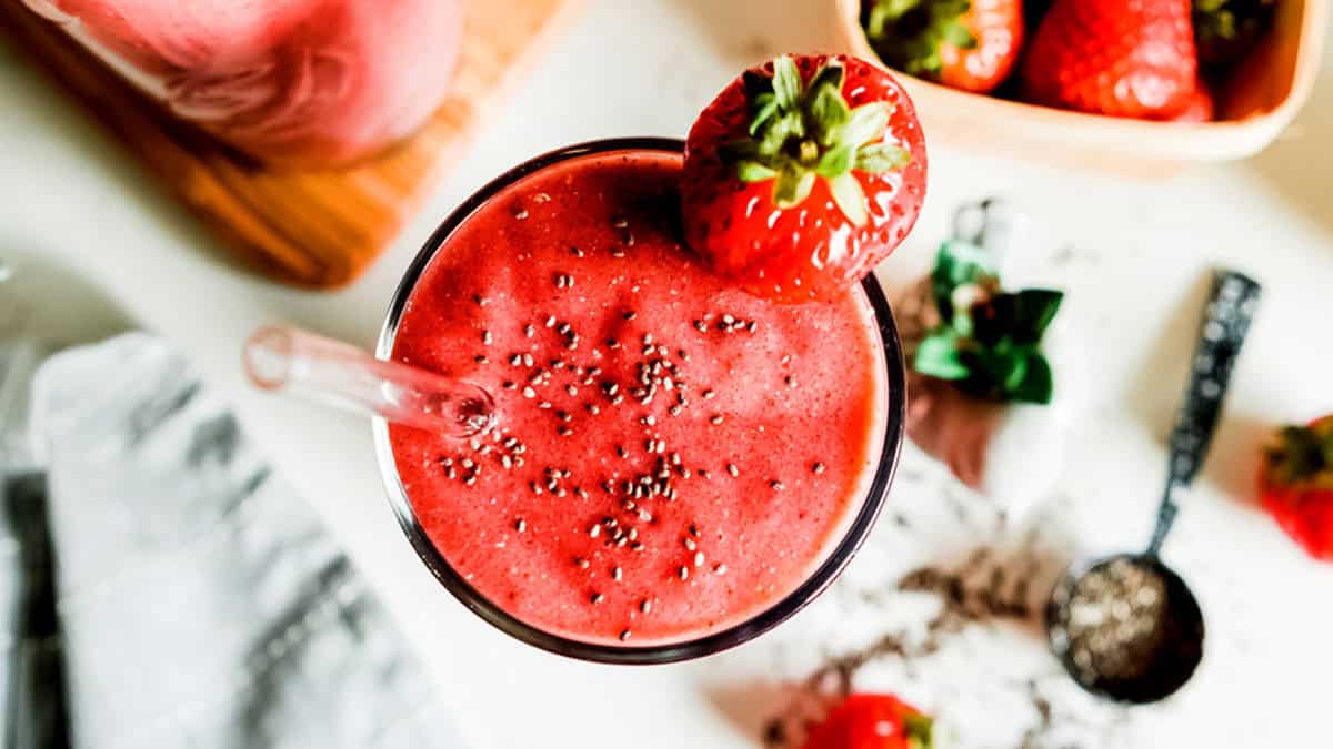 Refreshing strawberry smoothie in a glass with a straw, topped with a strawberry.