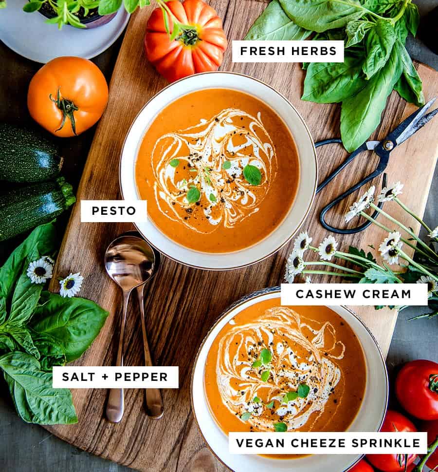 vegan tomato soup with text showing good soup toppings including fresh herbs, pesto, cashew cream, salt and pepper and vegan parmesan cheese.