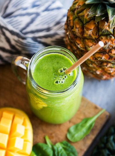 Tropical detox smoothie in a mason jar surrounded by fresh ingredients.