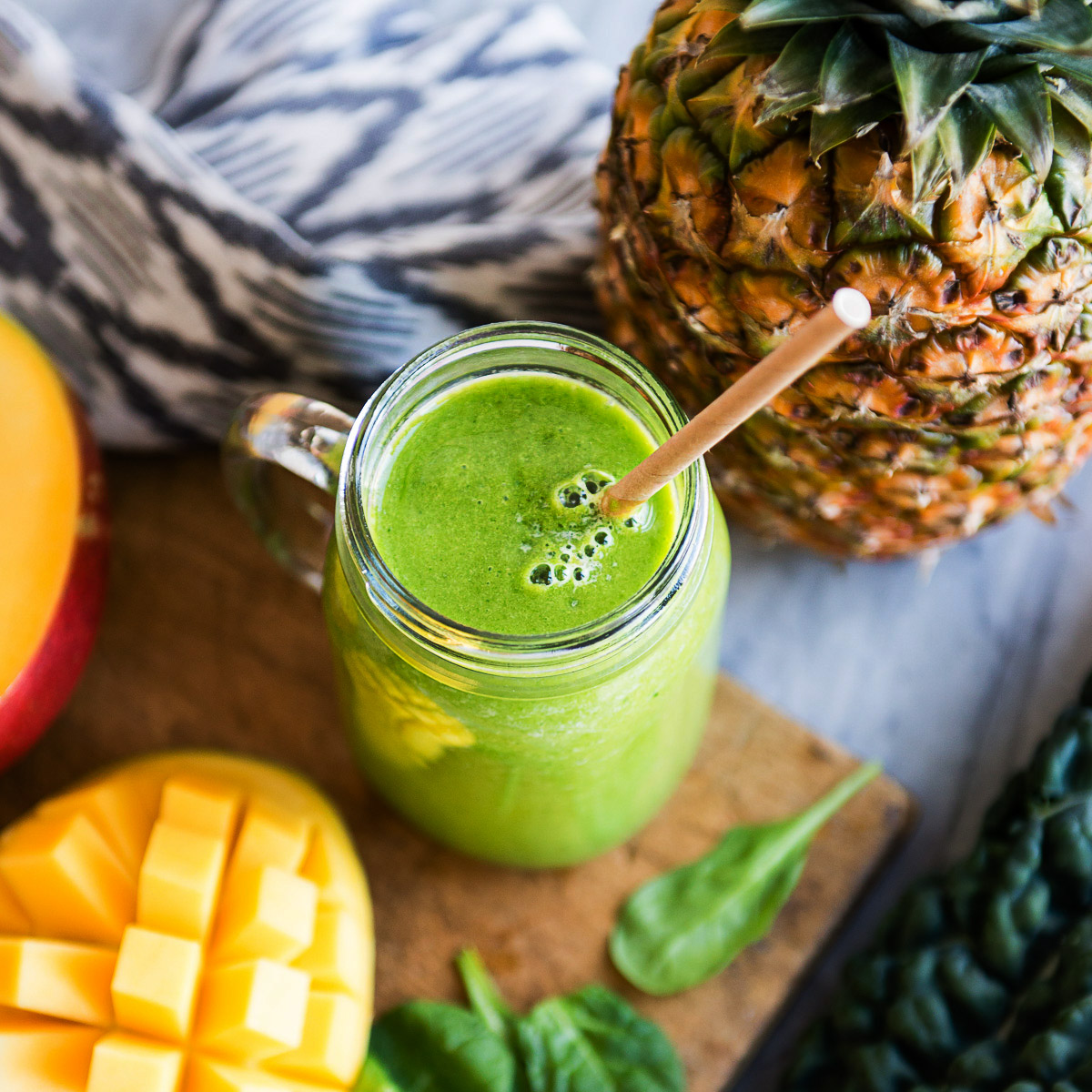 Tropical detox smoothie in a mason jar surrounded by fresh ingredients.