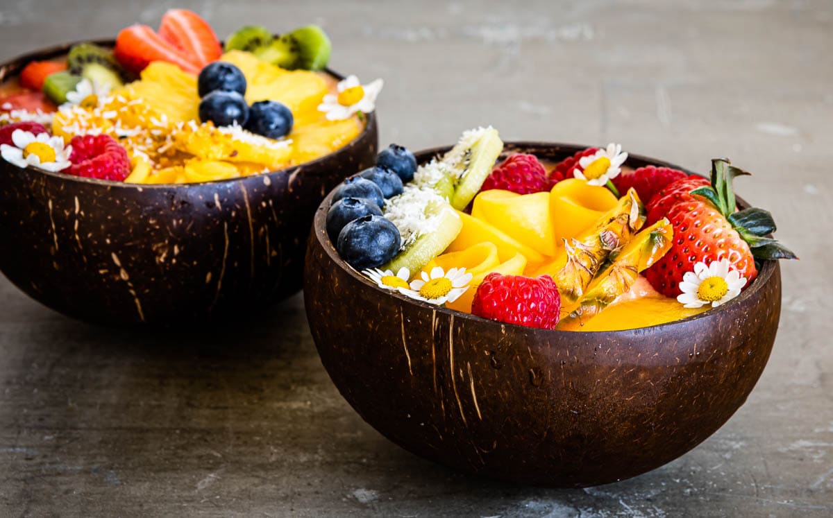 2 coconut bowls filled with a mango smoothie bowl recipe.