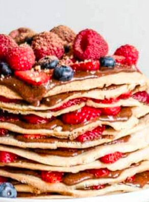 Layered crepes with nutella and fresh berries in between the layers and fresh strawberries in a bowl.