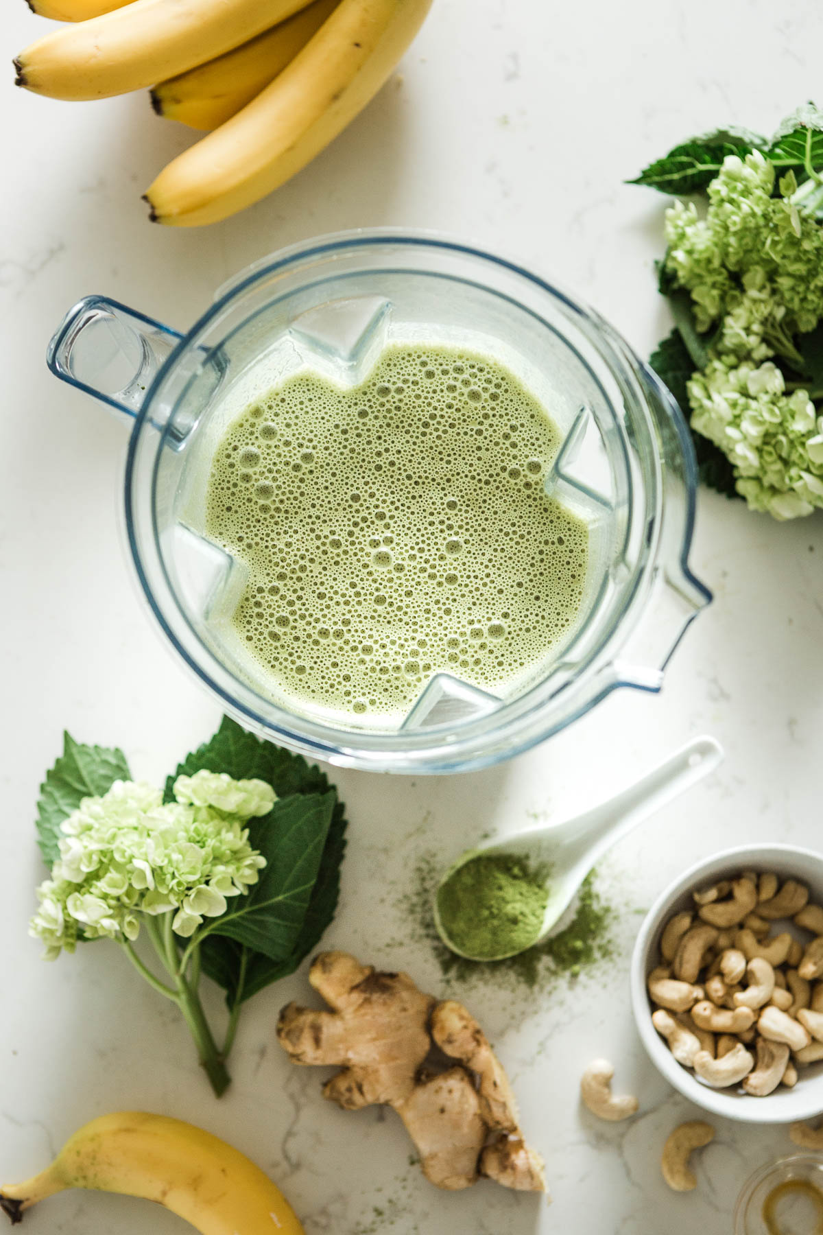 A matcha smoothie in a blender surrounded by ingredients.