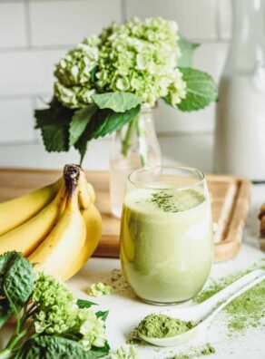 A matcha smoothie accompanied by bananas, matcha powder and hydrangeas