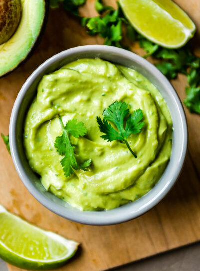 Vegan avocado crema in a glass bowl topped with cilantro, sliced jalapeño.