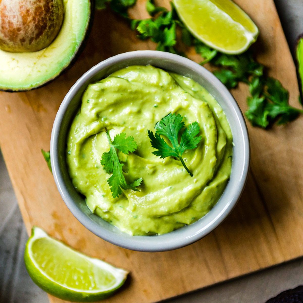 Vegan avocado crema in a glass bowl topped with cilantro, sliced jalapeño.