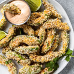 vegan avocado fries on a white plate with a container of chipotle ranch dipping sauce.