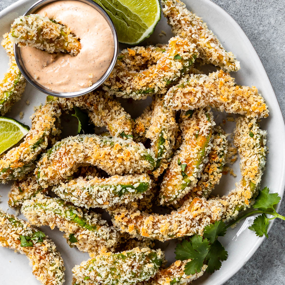 vegan avocado fries on a white plate with a container of chipotle ranch dipping sauce.