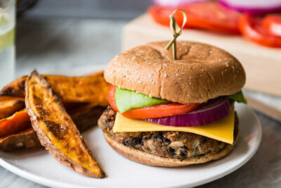 Vegan black bean burger on plate with red onion and tomatoes.