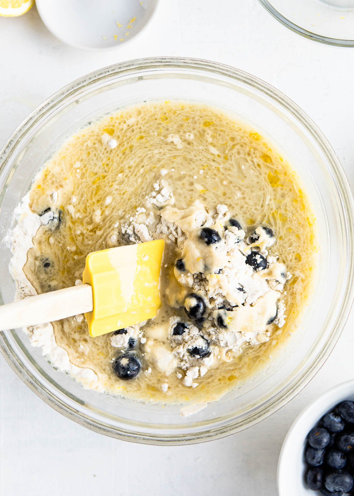 mixing the dry and wet ingredients together with a yellow spatula in a glass bowl.