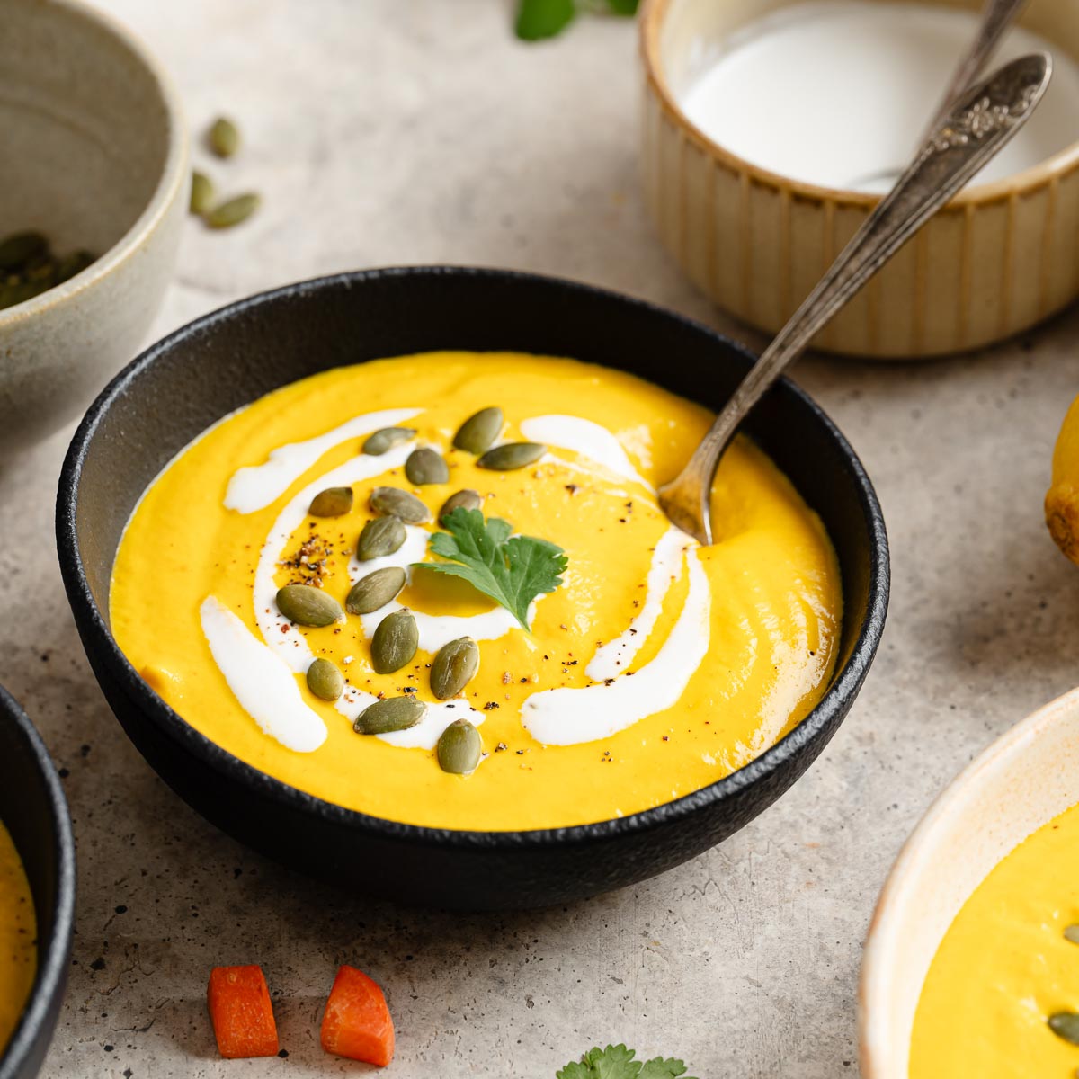 Carrot ginger Soup in a black bowl topped with swirls of cashew cream, fresh cilantro, and pepitas.