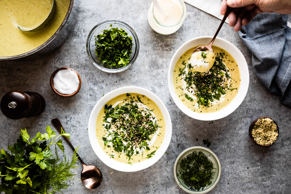 Table with two white celery soup bowls and toppings in small wood bowl.