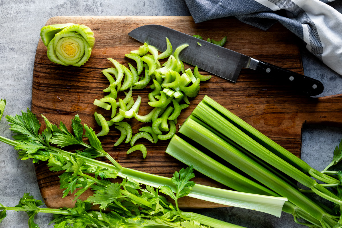 Walnut cutting board with chopped celery and stalks with leaves.