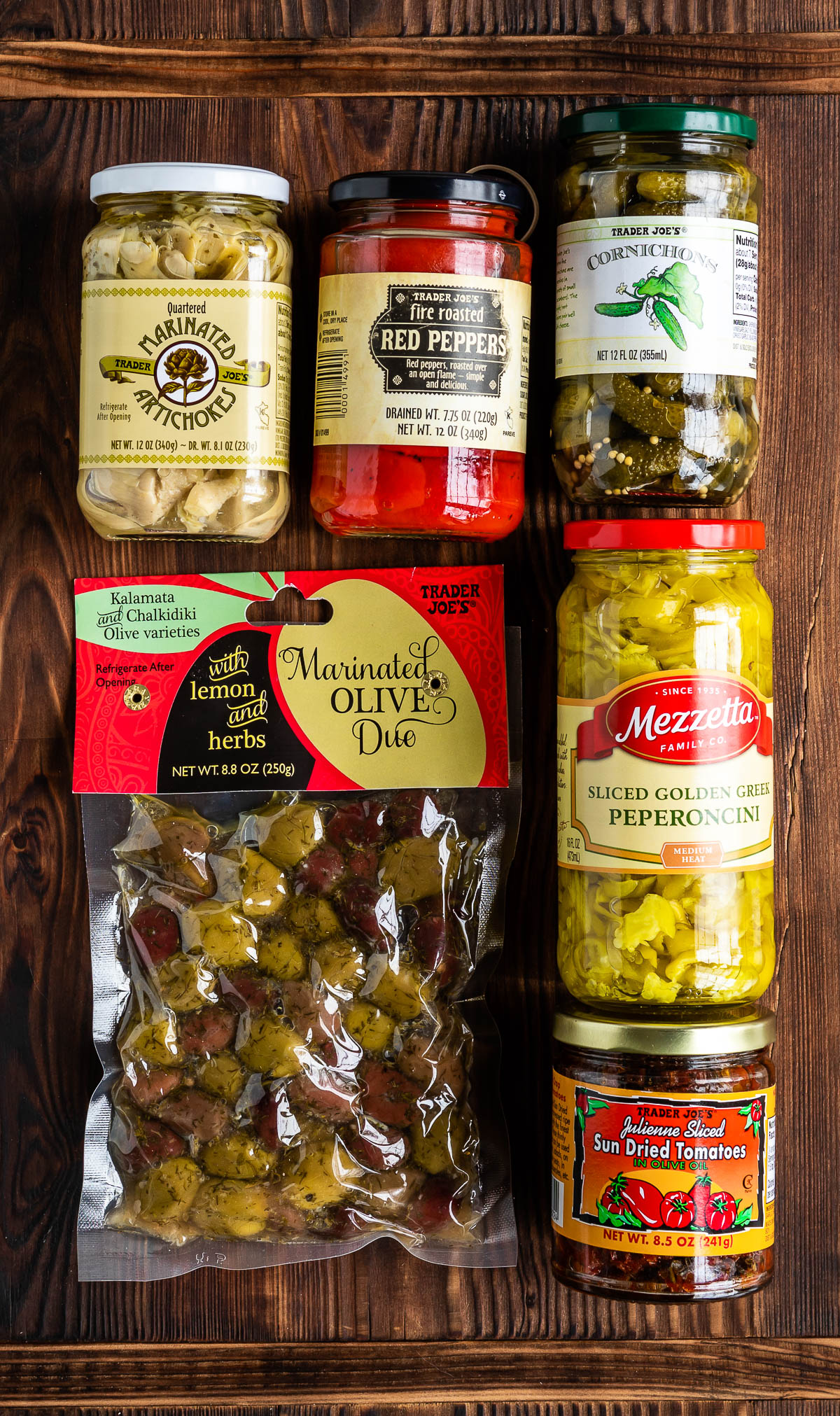 pickled vegetables in containers including marinated artichokes, roasted red peppers, cornichons, olives and peperoncini.