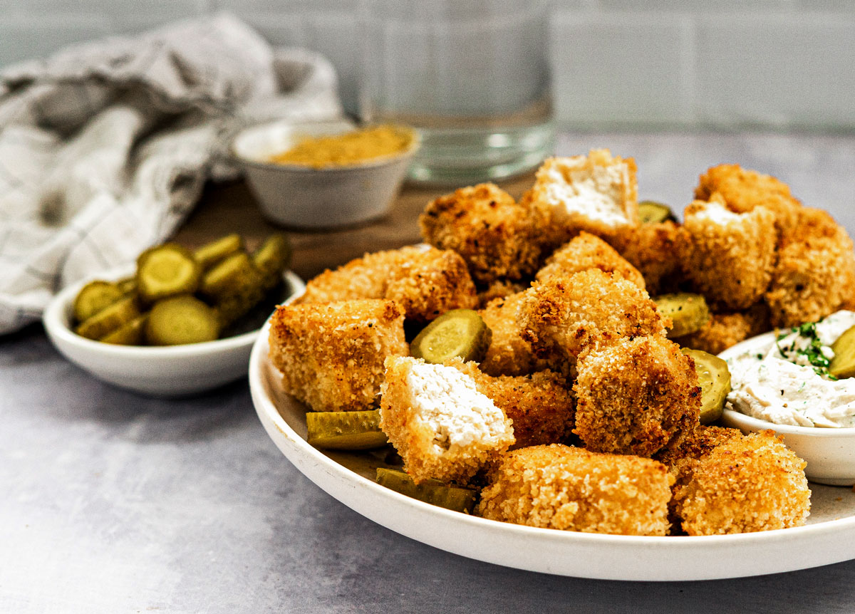 Vegan chicken nuggets piled high on a plate with sliced pickles.