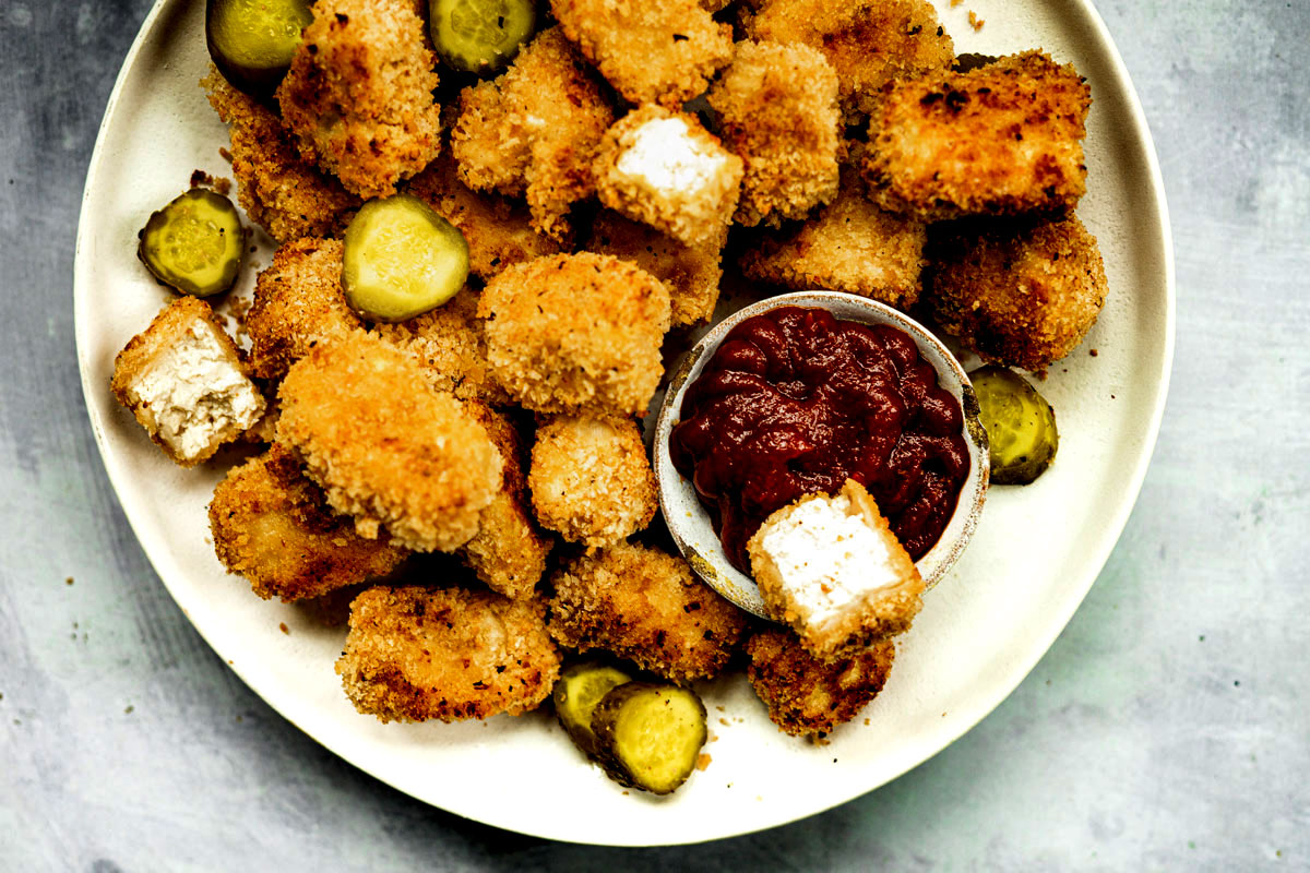 Crispy vegan chicken nuggets on a white plate with small bowl of ketchup.