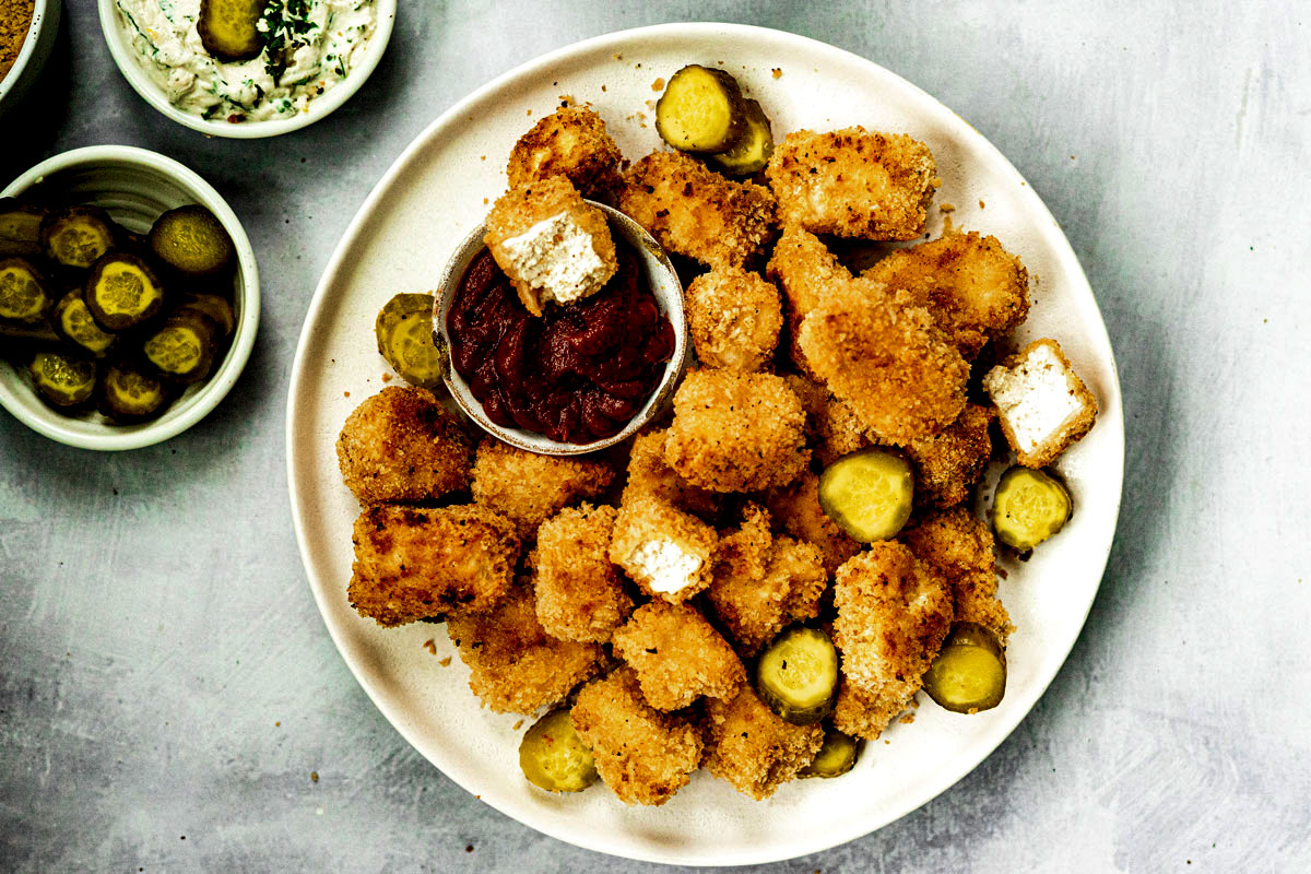 Plate piled high with vegan chicken nuggets, pickle slices and ketchup to dip.