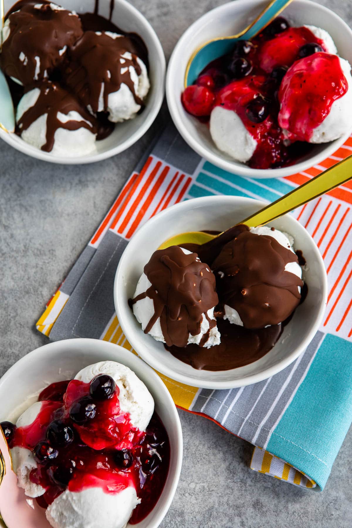 4 bowls of plant-based ice cream, some topped with chocolate crackle and some topped with fruit compote.