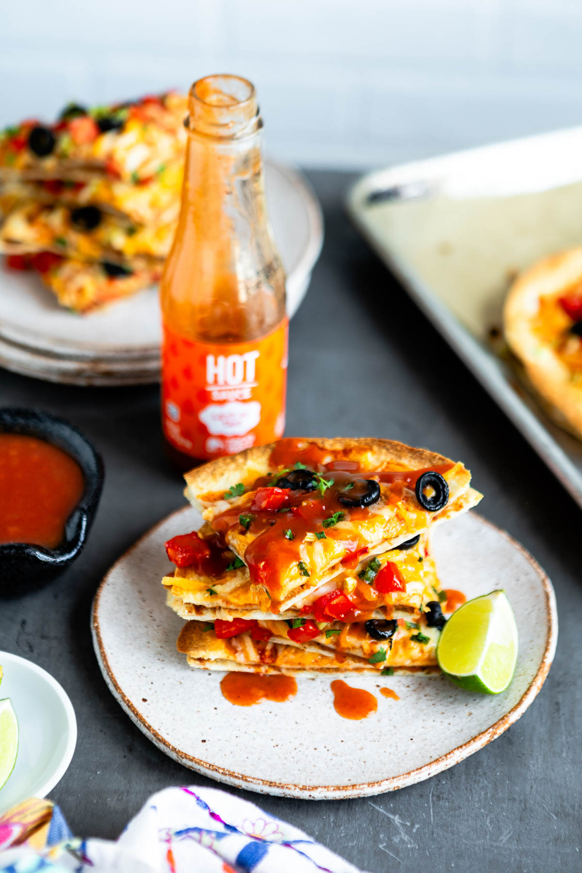 stack of vegan Mexican Pizza slices on a stone plate, topped with hot sauce and a lime wedge.