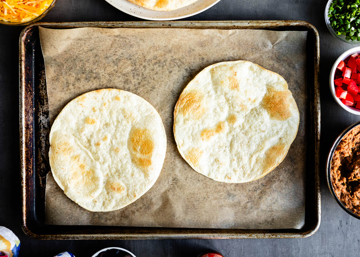 2 crispy tortilla shells on parchment lined baking sheet.